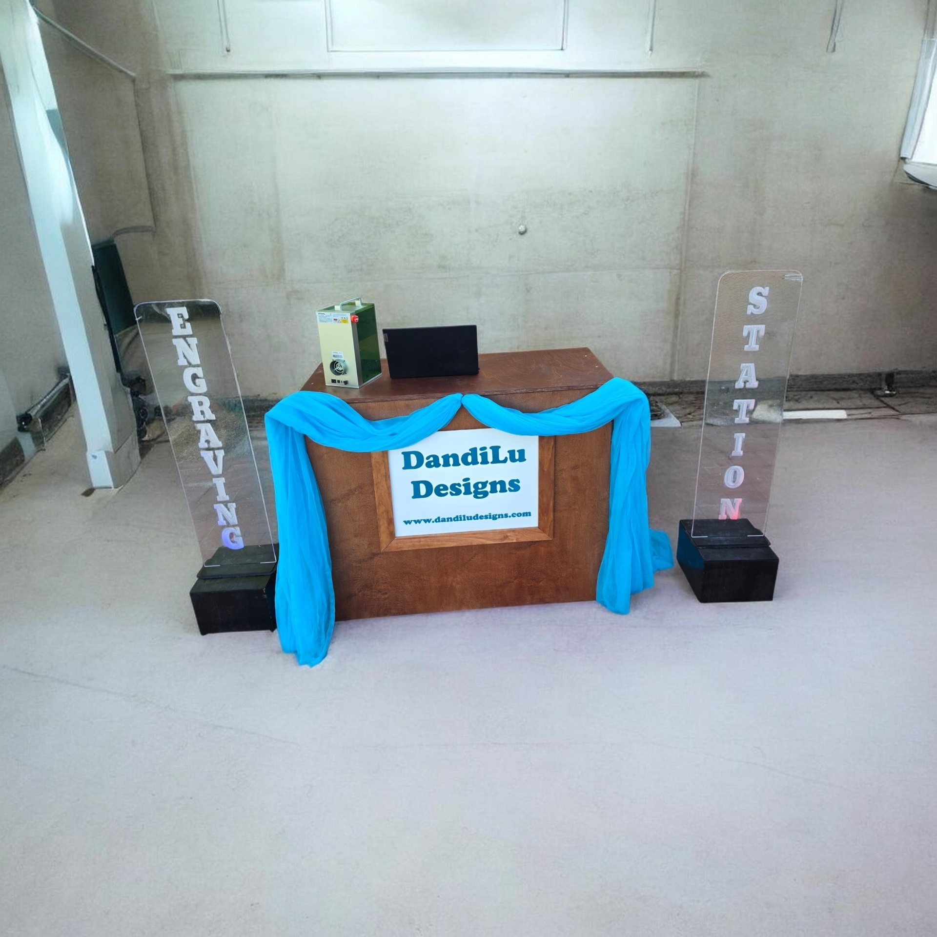 DandiLu Designs engraving station setup with signage and event draping